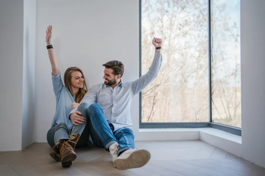 Casal sentado no chão de casa nova a celebrar aprovação de crédito com garantia pública do Estado, em banner da Maxfinance Presidente Lourinhã.